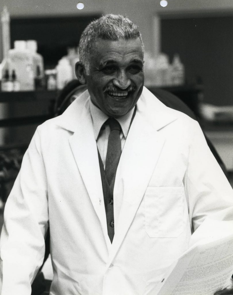 Samuel P. Massie dressed in a white lab coat smiles in a laboratory